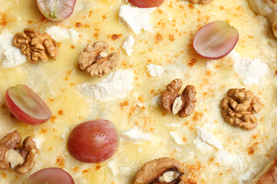 Photo of Delicious cheese pizza with walnuts and grapes as background, closeup
