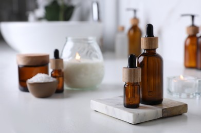 Essential oils and other cosmetic products on white countertop in bathroom