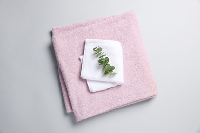 Soft folded towels with eucalyptus branch on light grey background, top view