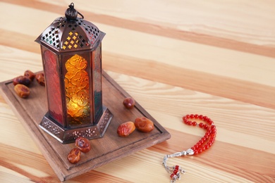 Muslim lantern Fanous, dried dates and prayer beads on wooden table. Space for text