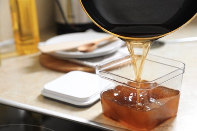 Photo of Pouring used cooking oil from frying pan into container on beige table in kitchen, closeup