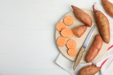 Whole and cut ripe sweet potatoes on white wooden table, flat lay. Space for text