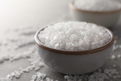 Bowls of natural sea salt on grey table, closeup