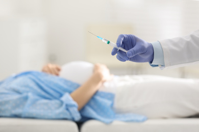 Doctor with syringe near pregnant woman in hospital, closeup. Vaccination concept