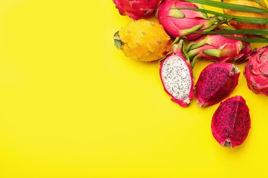 Different pitahaya fruits and palm leaf on yellow background, flat lay. Space for text
