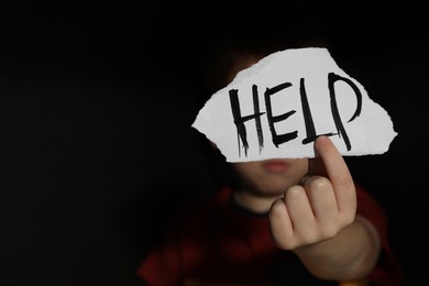 Photo of Little boy holding piece of paper with word Help on black background, space for text. Domestic violence concept