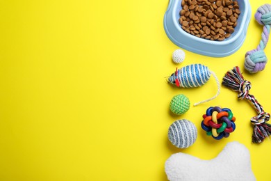 Feeding bowl and toys for pet on yellow background, flat lay. Space for text