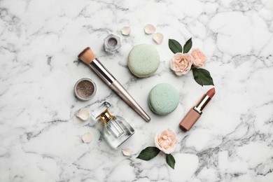 Flat lay composition with makeup products, roses and macarons on white marble background