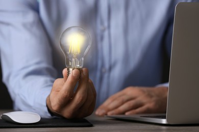 Glow up your ideas. Closeup view of man holding light bulb while working at wooden desk
