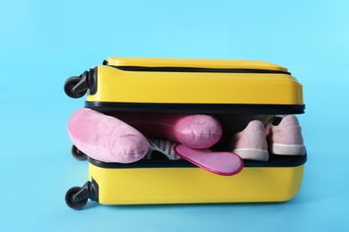 Yellow suitcase and travel pillow on light blue background