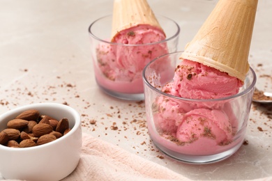 Delicious pink ice cream in wafer cones with almonds on light table, closeup