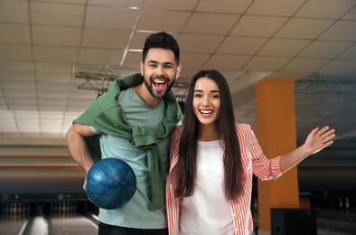 Happy young couple with ball in bowling club