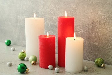 Burning candles with Christmas baubles on light grey table