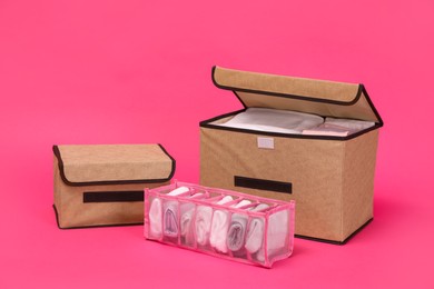 Textile storage cases and organizer with folded clothes on pink background