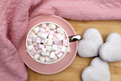 Photo of Cup of tasty cocoa with marshmallows, pink sweater and cookies on wooden table, flat lay