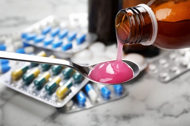 Pouring cough syrup from bottle into spoon on blurred background, closeup