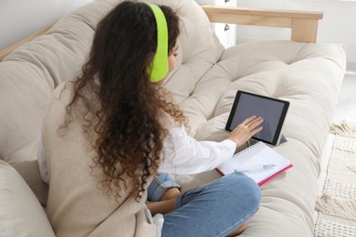 African American woman with headphones and tablet studying on sofa at home. Distance learning