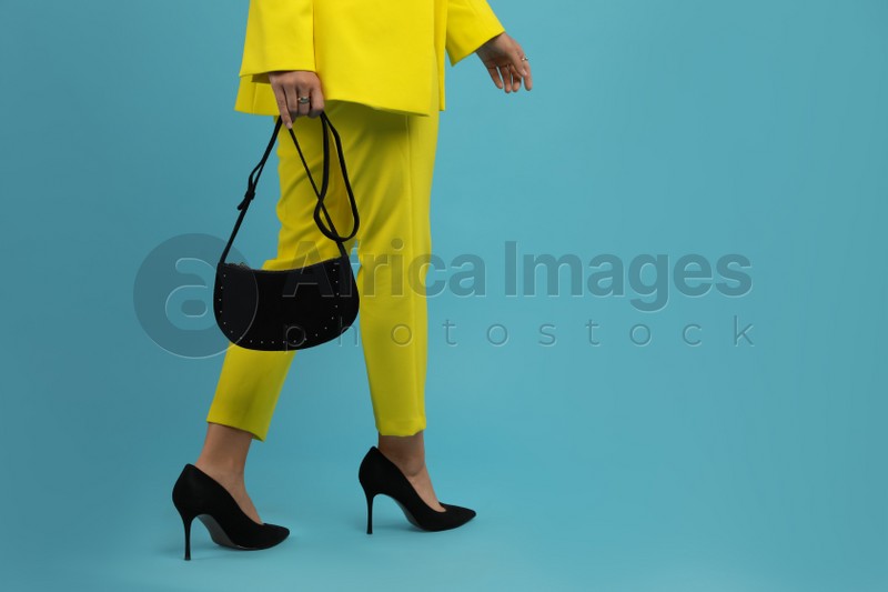 Fashionable woman with stylish bag on light blue background, closeup. Space for text