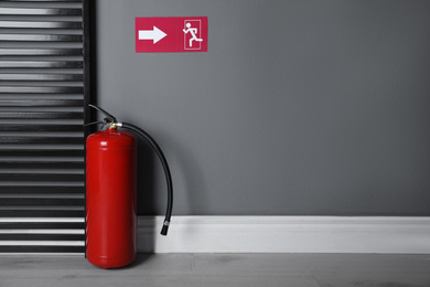 Fire extinguisher and emergency exit sign indoors. Space for text