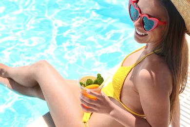 Woman with glass of refreshing drink near swimming pool, closeup