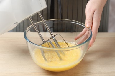 Woman beating eggs with mixer at wooden table, closeup
