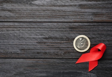 Red ribbon and condom on black wooden background, flat lay with space for text. AIDS disease awareness