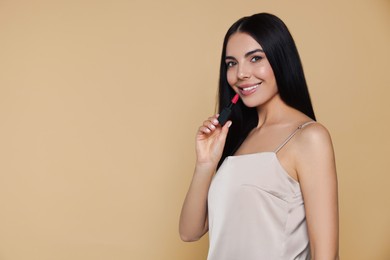 Photo of Young woman with beautiful makeup holding nude lipstick on beige background, space for text
