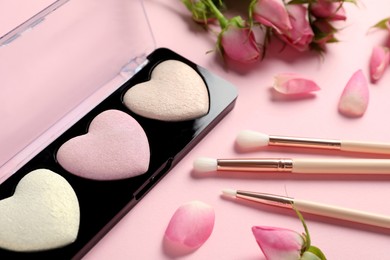 Photo of Palette of heart shaped eyeshadows with brushes and roses on light pink background