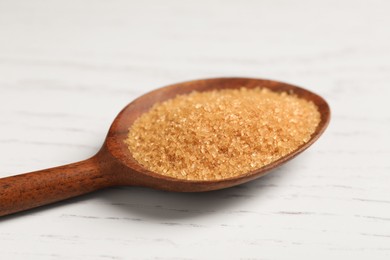 Spoon with brown sugar on white wooden table, closeup