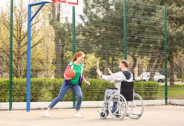 Man in wheelchair and young woman playing basketball on sports ground