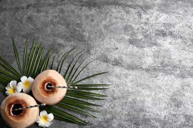 Photo of Young peeled coconuts with straws, tropical leaf and flowers on grey table, flat lay. Space for text