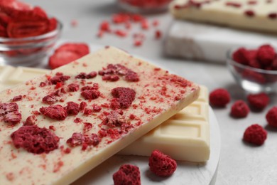 Photo of Chocolate bars with freeze dried raspberries on light marble table, closeup