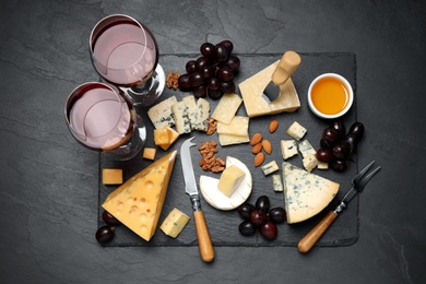 Cheese platter with specialized knife and fork on black table, flat lay