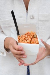 Woman holding paper box of takeaway noodles with fork, closeup. Street food