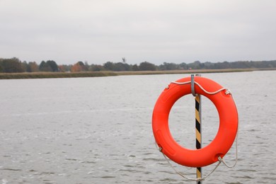 Photo of Orange lifebuoy hanging near sea outdoors, space for text. Real estate