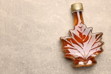 Leaf shaped bottle of tasty maple syrup on light grey table, top view. Space for text
