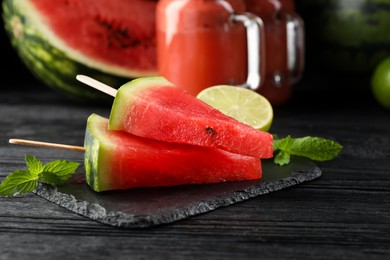 Slate board with cut juicy watermelon and lime on black wooden table