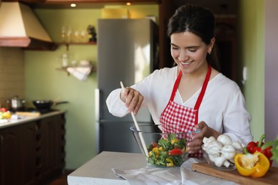 Young woman preparing salad at countertop in kitchen, space for text