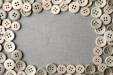 Frame of plastic sewing buttons on grey fabric, flat lay. Space for text