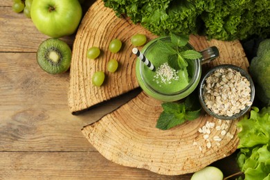 Photo of Mason jar of fresh green smoothie with ingredients on wooden table, flat lay