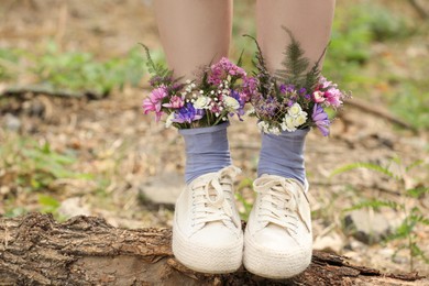 Woman standing on log with flowers in socks outdoors, closeup