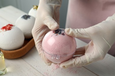 Photo of Woman in gloves making bath bomb at white table , closeup