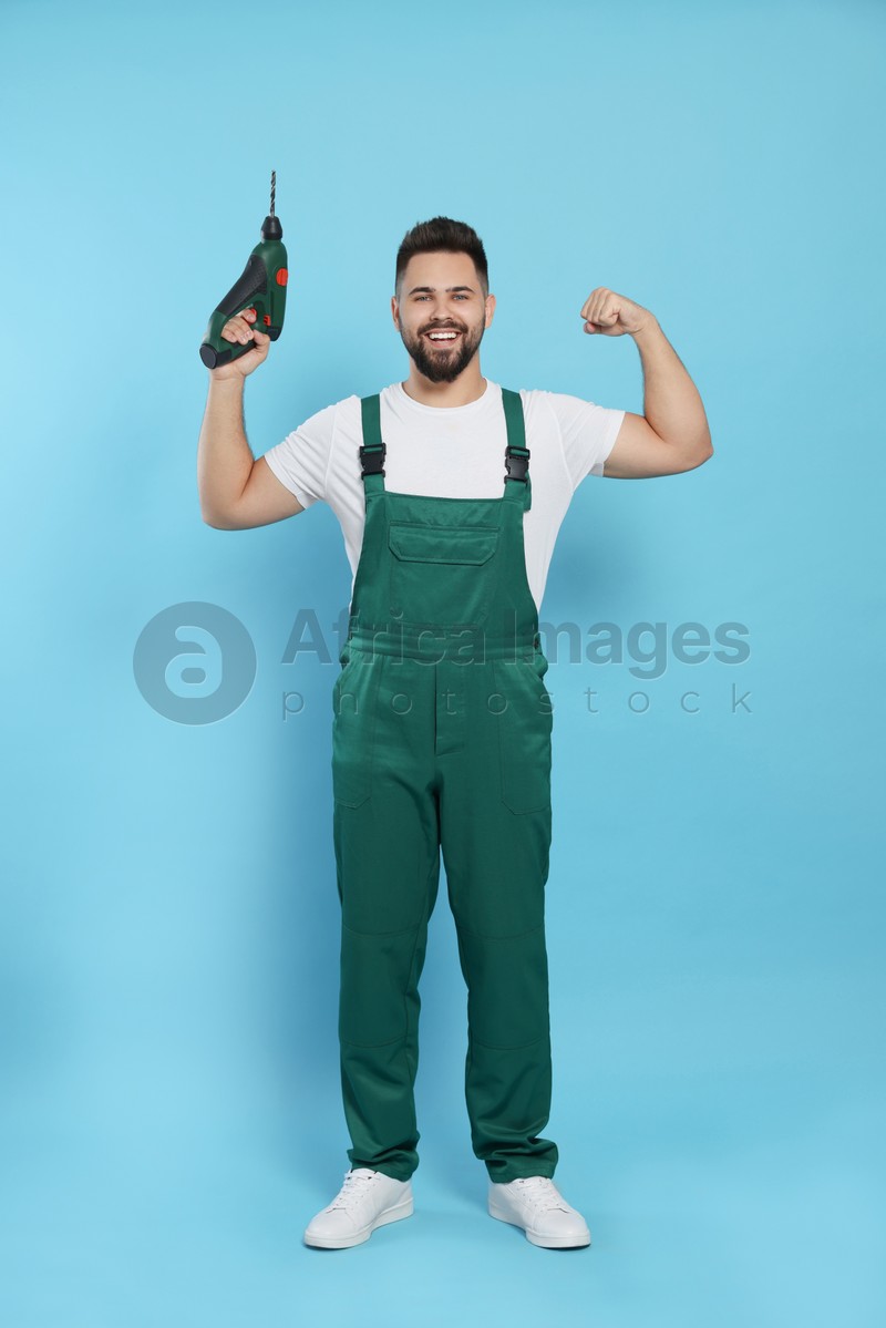 Young worker in uniform with power drill on light blue background