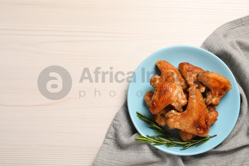 Plate with delicious fried chicken wings and sprig of rosemary on white wooden table, top view. Space for text