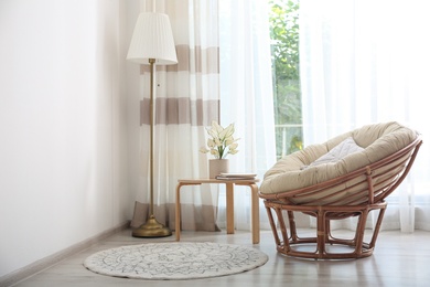Comfortable papasan chair near window with stylish curtains in living room. Interior design