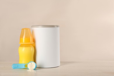 Blank can of powdered infant formula, feeding bottle and scoop on white wooden table, space for text