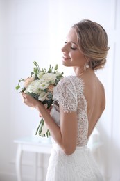 Young bride with elegant hairstyle holding wedding bouquet indoors