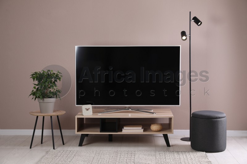 Photo of Modern TV on stand near pale pink wall indoors. Interior design