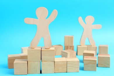 Wooden cubes and human figures on light blue background. Social roles concept