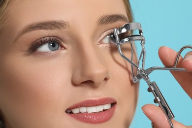 Photo of Young woman using eyelash curler on light blue background, closeup